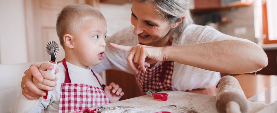 Un enfant handicapé trisomique heureux avec sa mère à l'intérieur en train de faire de la pâtisserie.