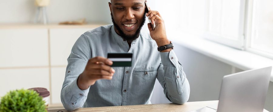 Homme d'affaires noir tenant une carte de crédit et parlant au téléphone portable au bureau