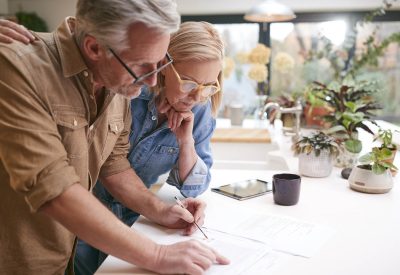 Couple mature revoyant et signant les finances domestiques et les documents d'investissement dans la cuisine, à la maison